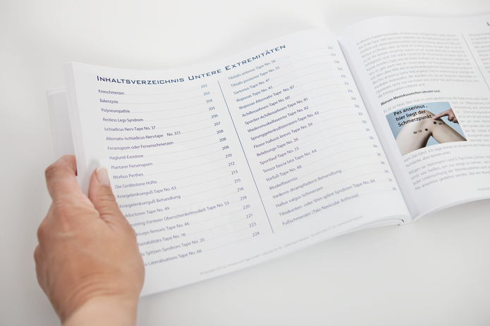 Jemand blättert in einem medizinischen Kursbuch mit Inhaltsverzeichnis zu Kinesiologie-Taping.